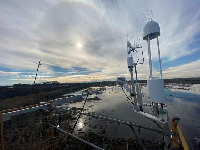 Tower-top flux and radiation sensors over a flooded field with an ice halo around the sun in the background