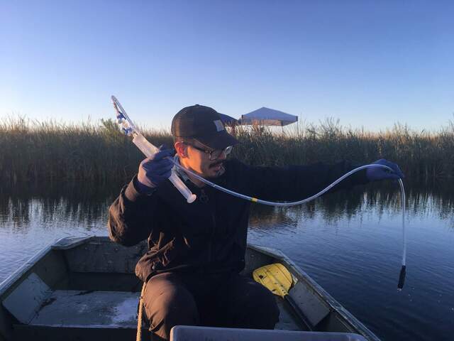 Carlos is sampling at the center of the channel using a syringe-stopcock-tubing assembly